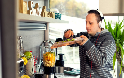 Image of man wearing headphones scraping food off a chopping board into an electric blender.